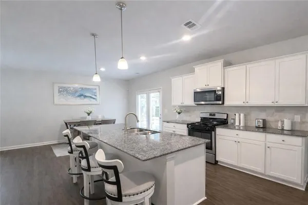 a kitchen with stainless steel appliances granite countertop a stove a sink a microwave a dining table and chairs with wooden floor