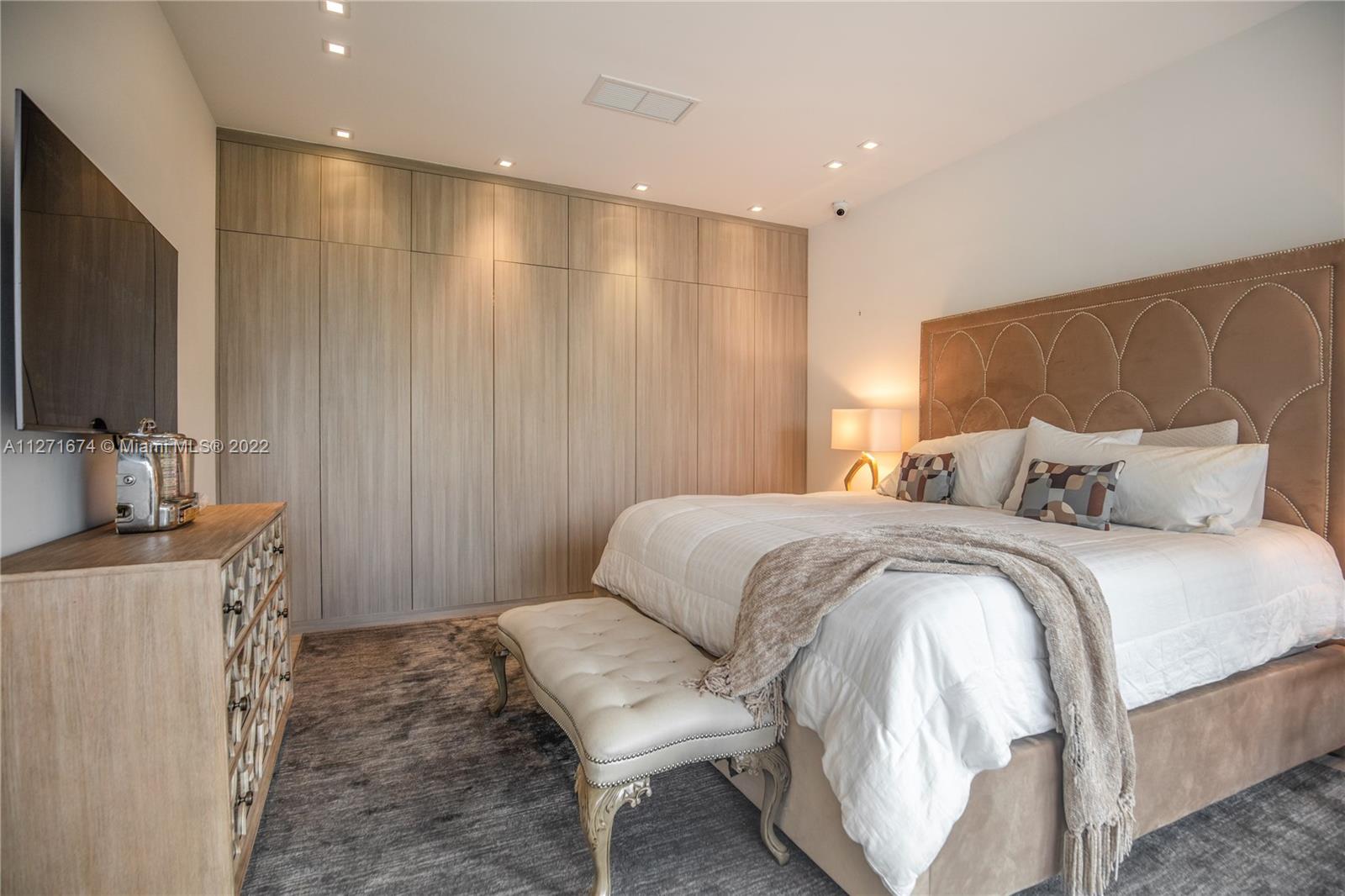 5061 North Bay Road Miami Beach, FL 33140 - Photo 17 of 23 a spacious bedroom with a bed a couch and a flat tv screen on the dresser