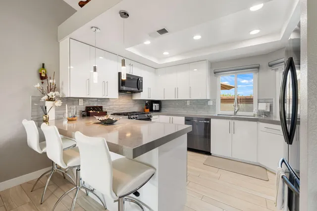 a kitchen with stainless steel appliances granite countertop a sink a stove a refrigerator cabinets and a dining table with chairs