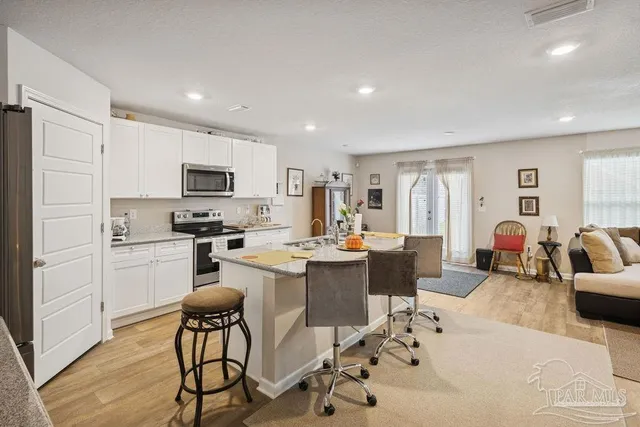 a living room with stainless steel appliances kitchen island granite countertop a refrigerator a stove a sink dishwasher a dining table and chairs with wooden floor