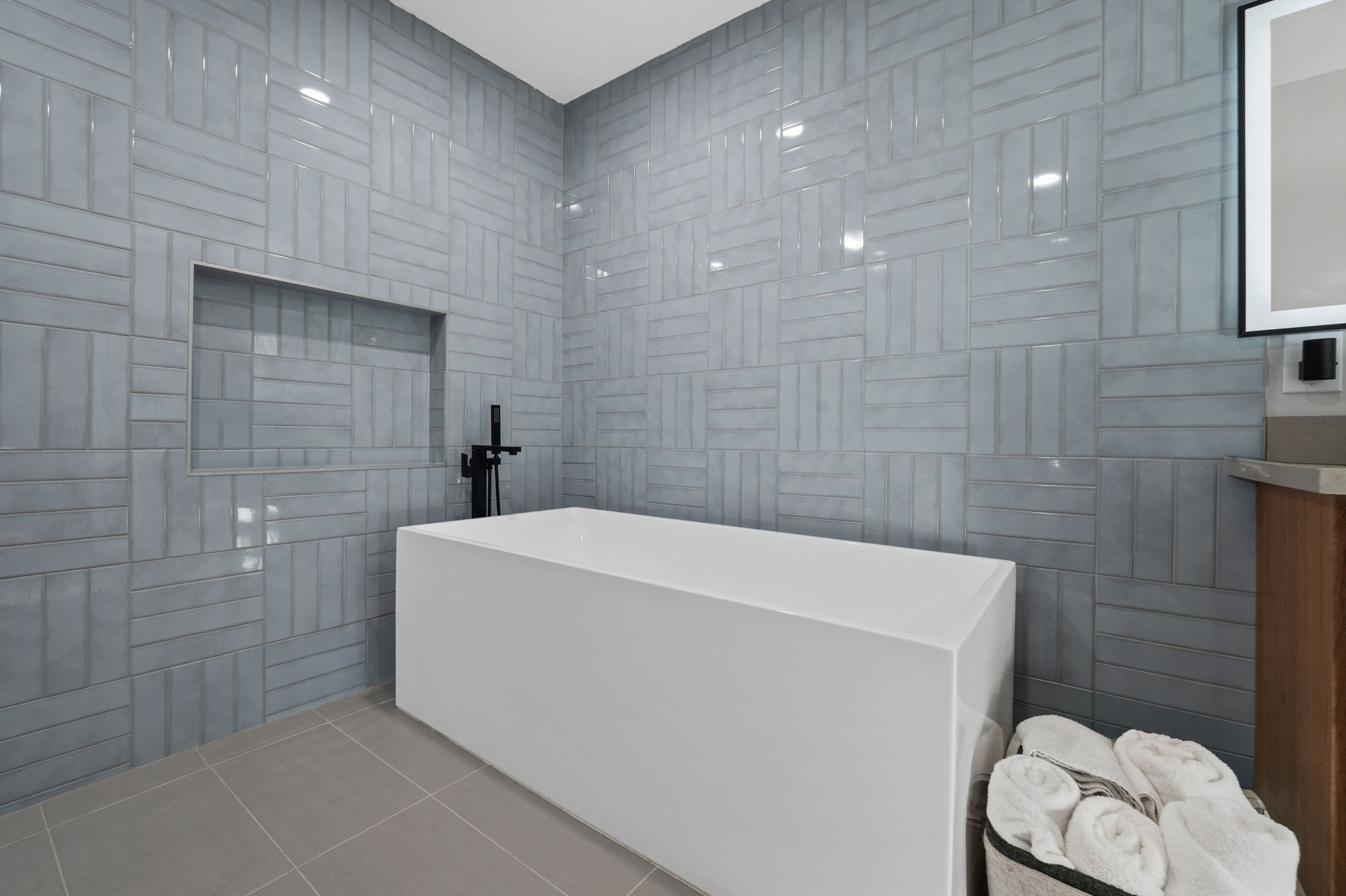 1831 Palm Street Houston, TX 77004 - Photo 13 of 27 The primary bathroom was recently renovated, and features a sleek freestanding bathtub against a modern, geometric gray tile wall. It includes a built-in niche for storage and a stylish black faucet, creating a clean and contemporary look.