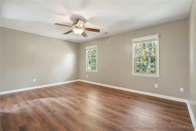 an empty room with wooden floor fan and windows
