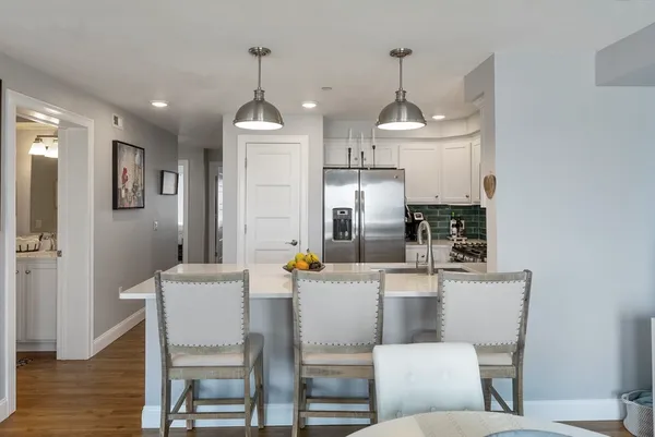 a kitchen with stainless steel appliances kitchen island granite countertop a dining table chairs and a refrigerator
