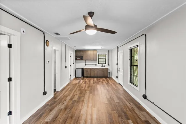 a big room with wooden floor a ceiling fan and windows