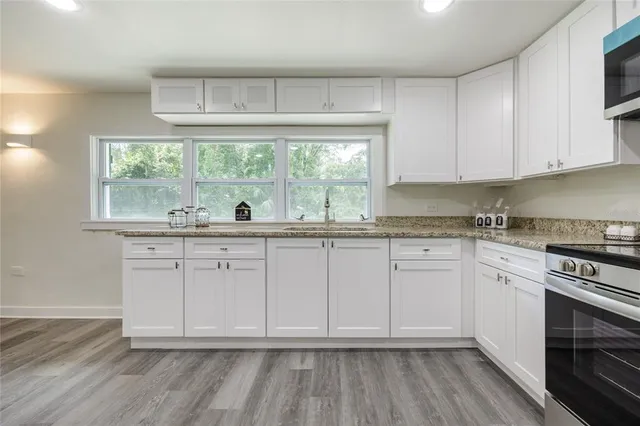 a kitchen with stainless steel appliances granite countertop a stove a sink and white cabinets with wooden floor