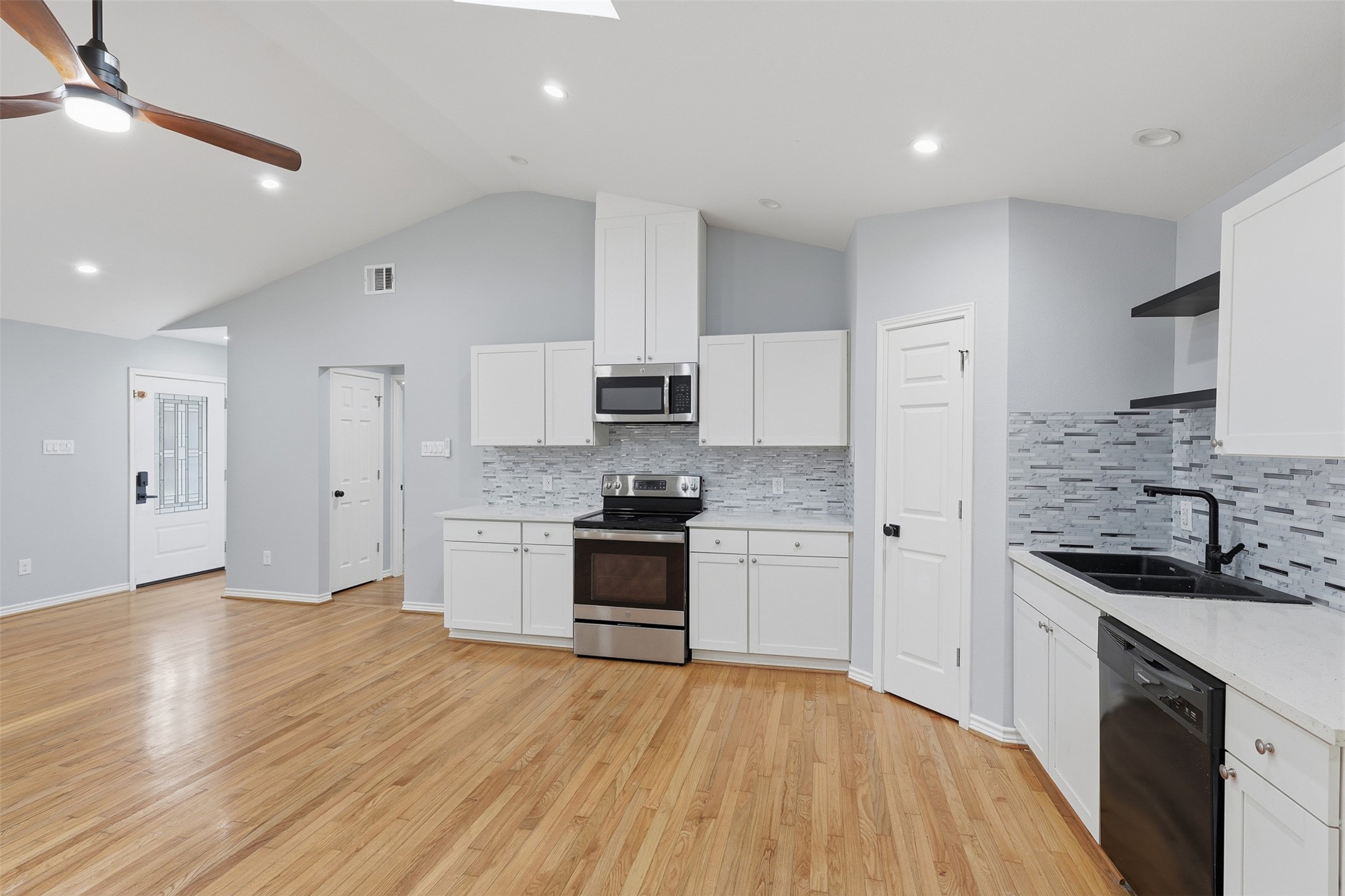 4926 Edfield Street Houston, TX 77033 - Photo 5 of 30 Spacious kitchen with modern stainless steel appliances, sleek white cabinetry, and a stylish tile backsplash, all complemented by warm hardwood floors and ample natural light.