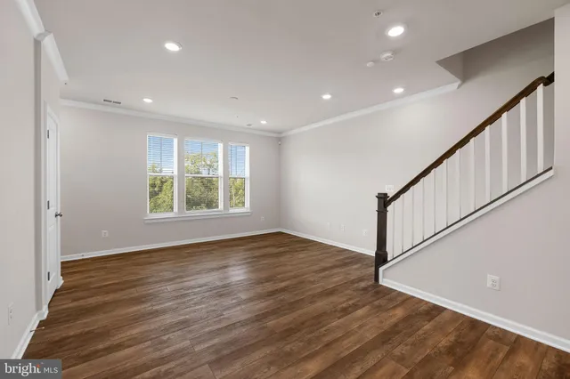 a view of an empty room with wooden floor and fan