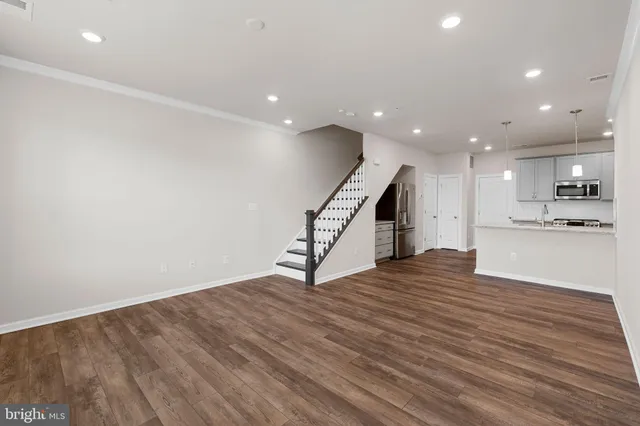 a view of an empty room with wooden floor kitchen and a window