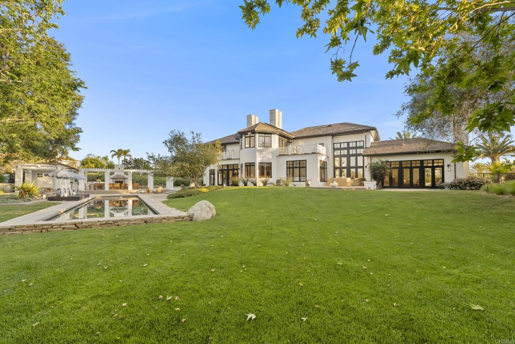 7891 Muirfield Way Rancho Santa Fe, CA 92067 - Photo 23 of 26 a view of a white house with a big yard and potted plants and large trees