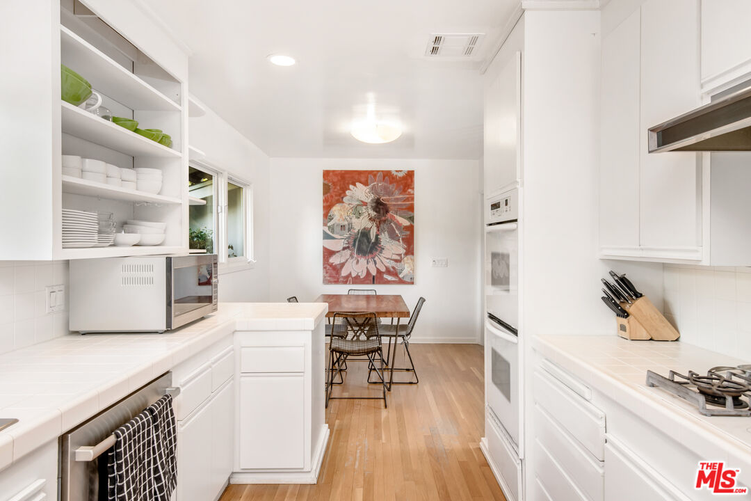 16849 Adlon Road Encino, CA 91436 - Photo 10 of 40 a kitchen with stainless steel appliances wooden floor and a table