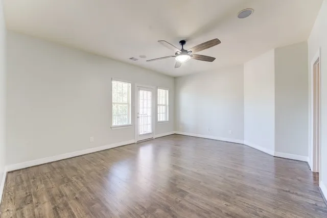 an empty room with wooden floor fan and windows