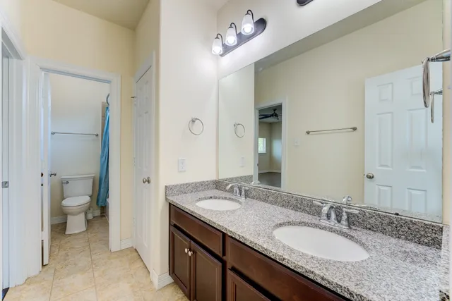 a bathroom with a granite countertop double vanity sink a mirror and a toilet