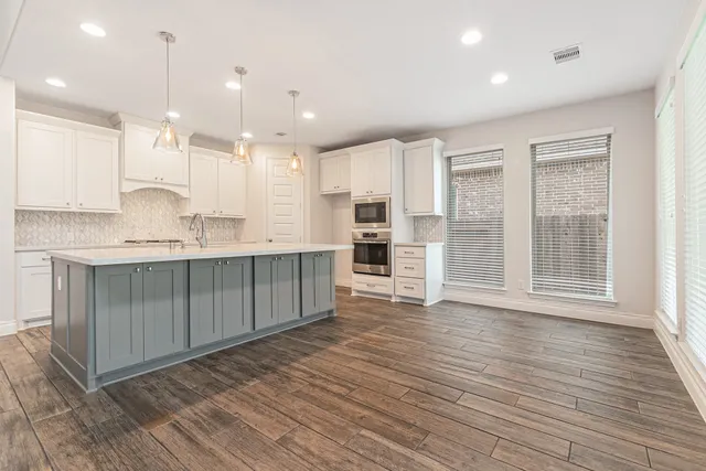 a large kitchen with stainless steel appliances granite countertop a stove a sink and white cabinets with wooden floor