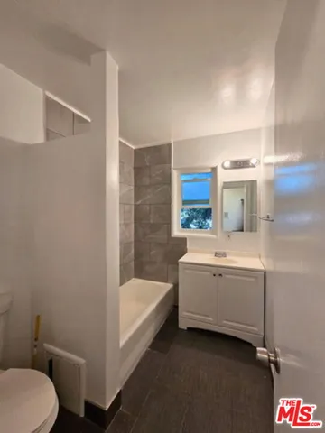 a bathroom with a granite countertop bathtub sink vanity mirror and toilet