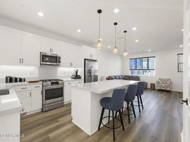 a kitchen with stainless steel appliances kitchen island granite countertop a stove a sink a refrigerator and a dining table with wooden floor