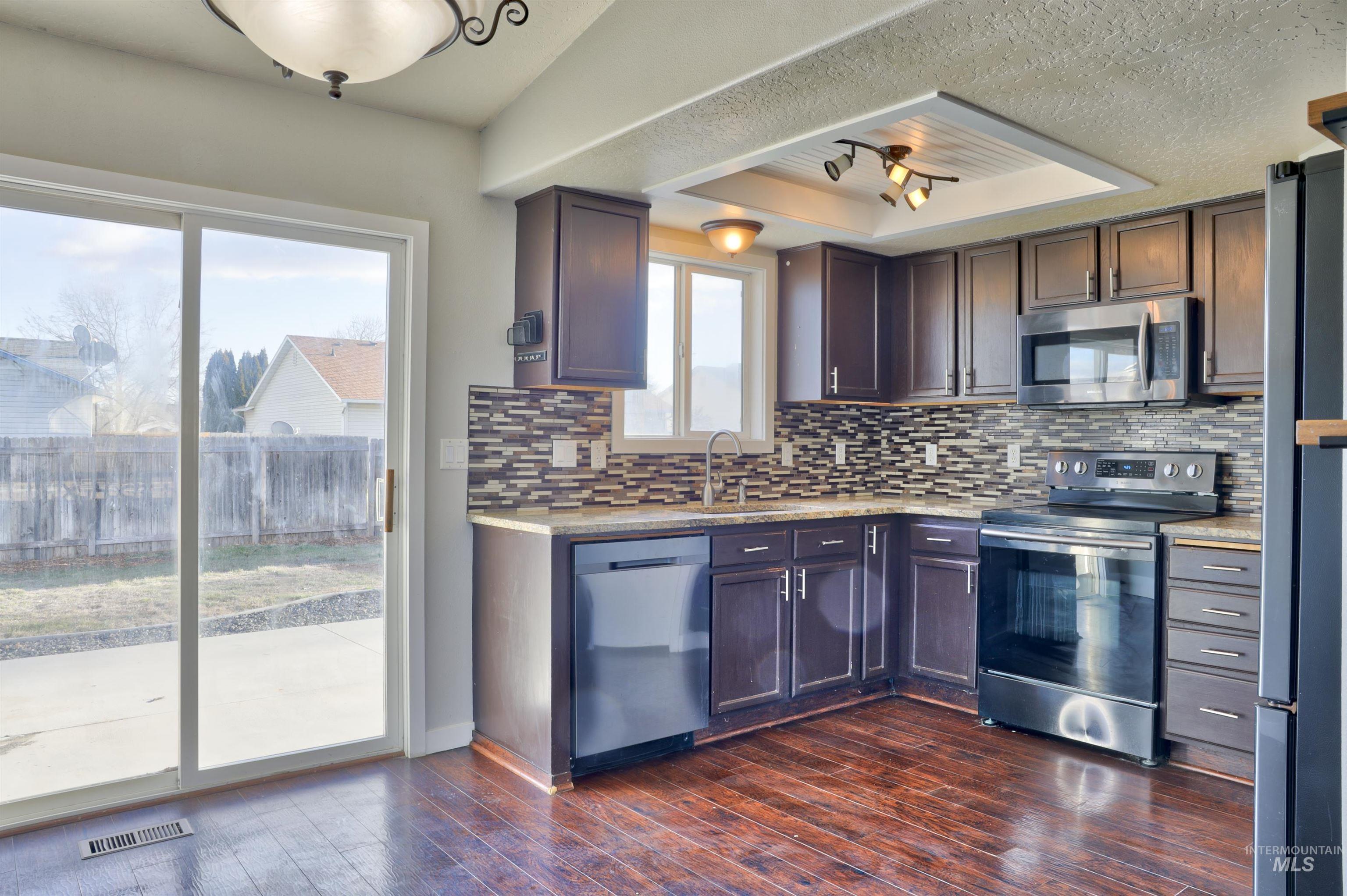 4911 Buffalo Grass Avenue Caldwell, ID 83607 - Photo 2 of 15 Kitchen with appliances with stainless steel finishes, light stone counters, dark wood-style floors, a tray ceiling, and backsplash