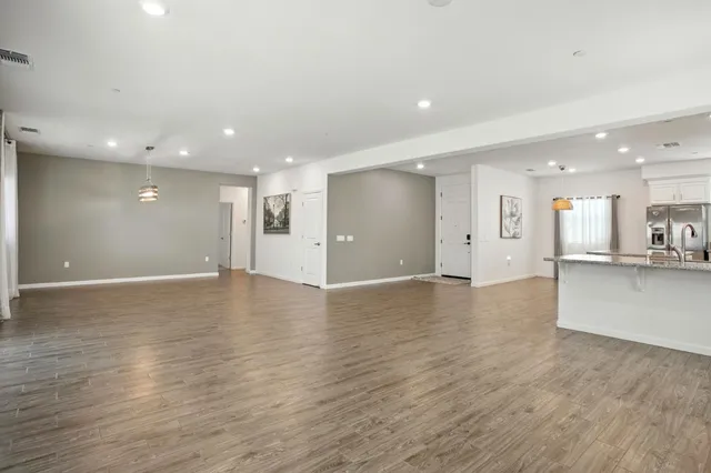 a view of an empty room with wooden floor and a kitchen