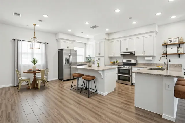 a kitchen with stainless steel appliances a dining table chairs stove refrigerator and cabinets