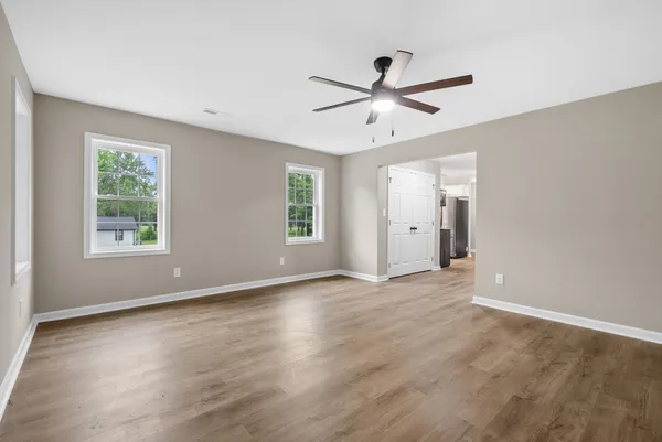 an empty room with wooden floor fan and windows
