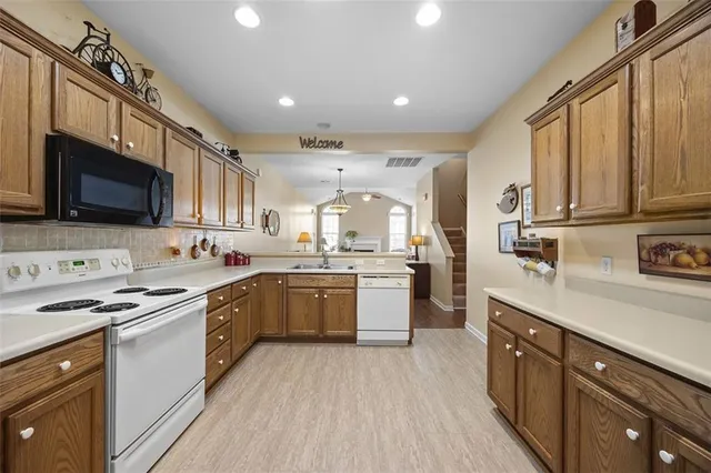 a kitchen with stainless steel appliances granite countertop a stove top oven a sink dishwasher and a refrigerator with wooden cabinets