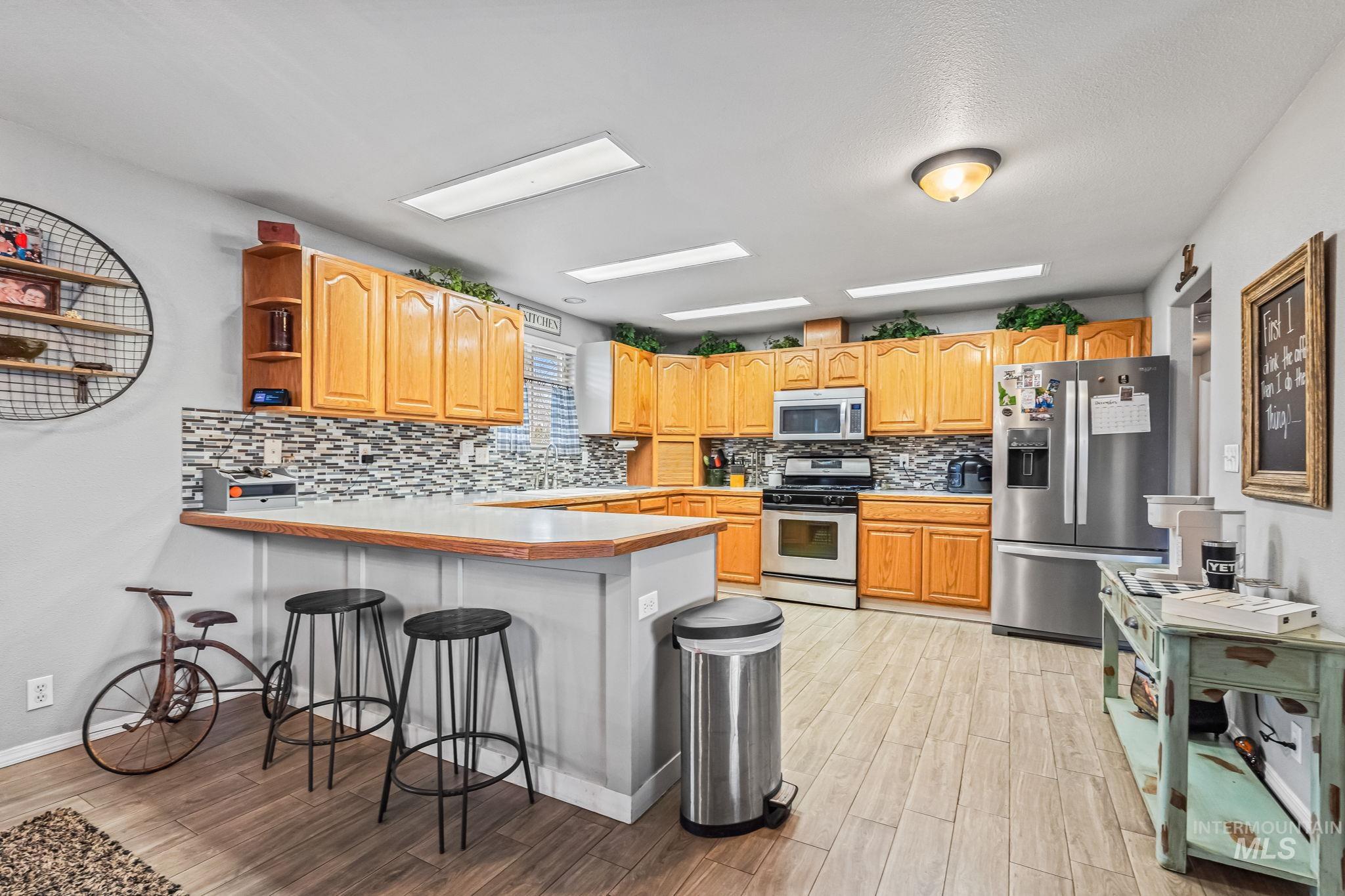 7650 West Colt Drive Boise, ID 83709 - Photo 11 of 30 Kitchen featuring appliances with stainless steel finishes, open shelves, a breakfast bar, a peninsula, and light wood finished floors