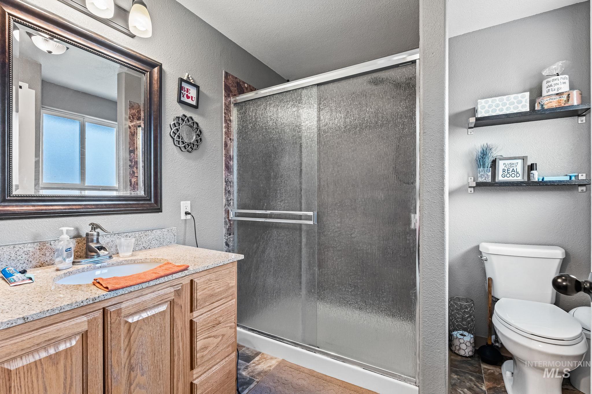 7650 West Colt Drive Boise, ID 83709 - Photo 19 of 30 Bathroom with a textured wall, vanity, a shower stall, stone tile flooring, and a textured ceiling