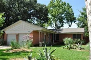 a view of a house with brick walls and a yard with plants and a large tree