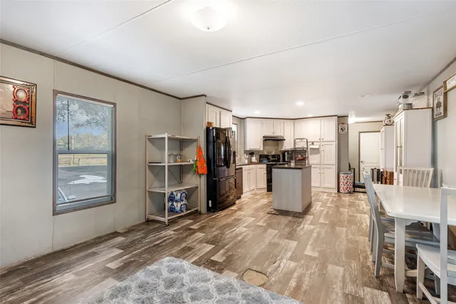 a kitchen with stainless steel appliances kitchen island granite countertop a refrigerator oven a sink dishwasher and white cabinets with wooden floor