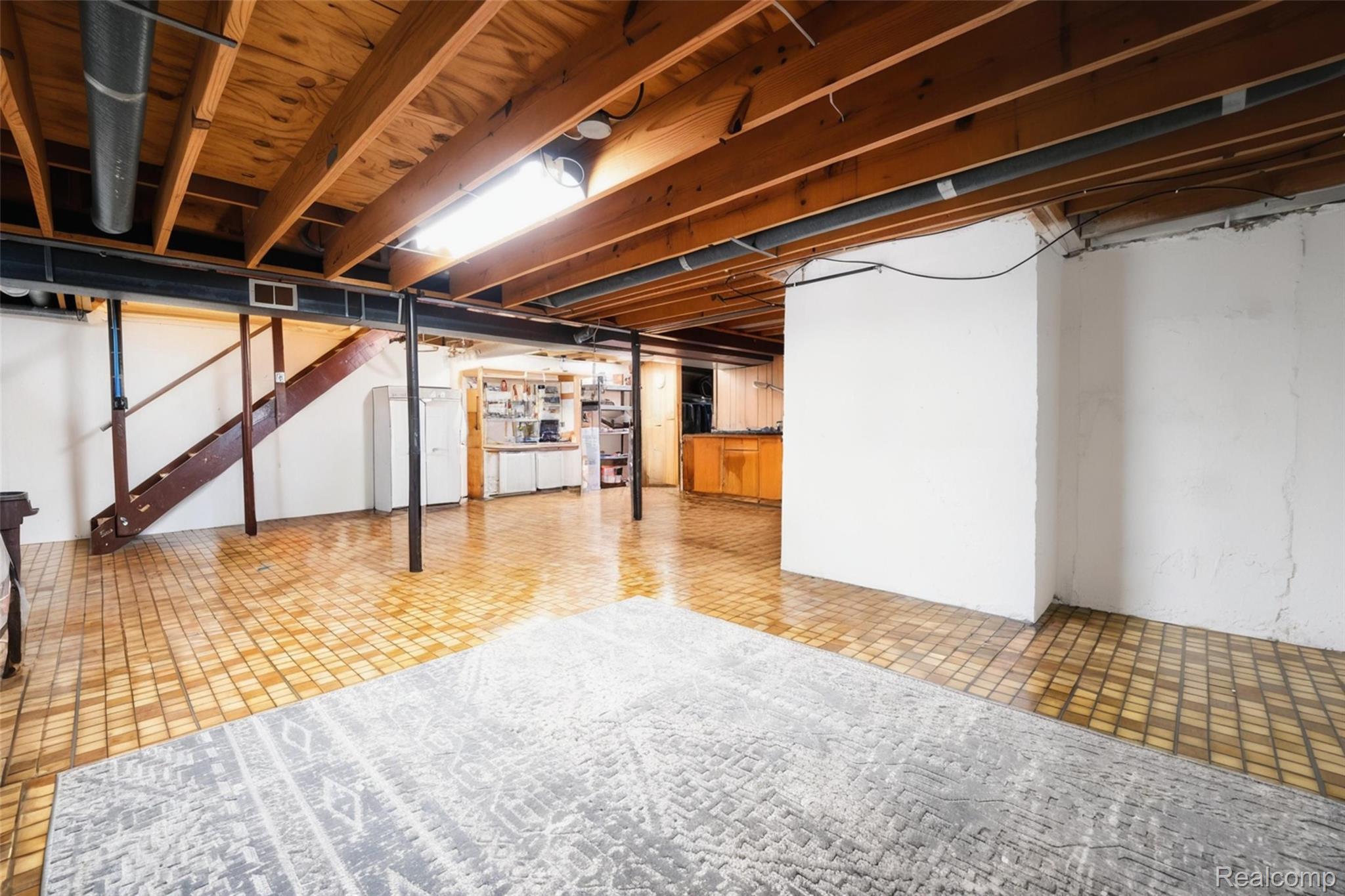 41768 Hanford Road Canton, MI 48187 - Photo 21 of 28 Expansive finished basement featuring exposed wood ceiling joists and support beams, a built-in wet bar with wooden cabinetry, a dedicated utility area with white cabinetry, and durable tile flooring throughout