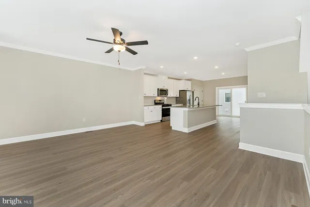 a view of a kitchen with wooden floor a ceiling fan and stainless steel appliances