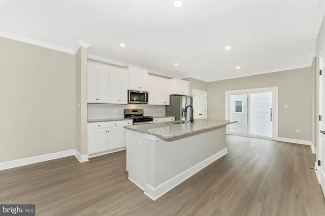 a large white kitchen with stainless steel appliances granite countertop a stove a sink a refrigerator and white cabinets with wooden floor