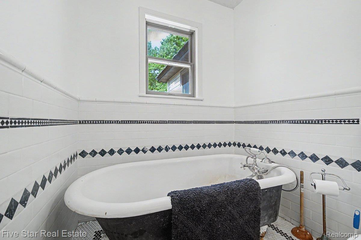 175 Bishop Road Sterling, MI 48659 - Photo 26 of 41 Bathroom featuring a classic clawfoot tub with chrome fixtures, white subway tile walls with black diamond accents, and a window providing natural light