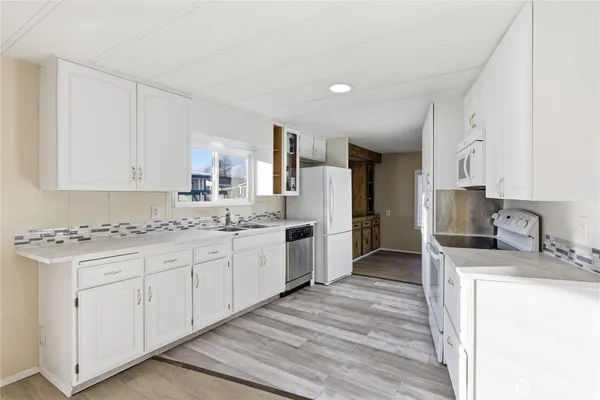 a kitchen with granite countertop a sink stove refrigerator and white cabinets with wooden floor