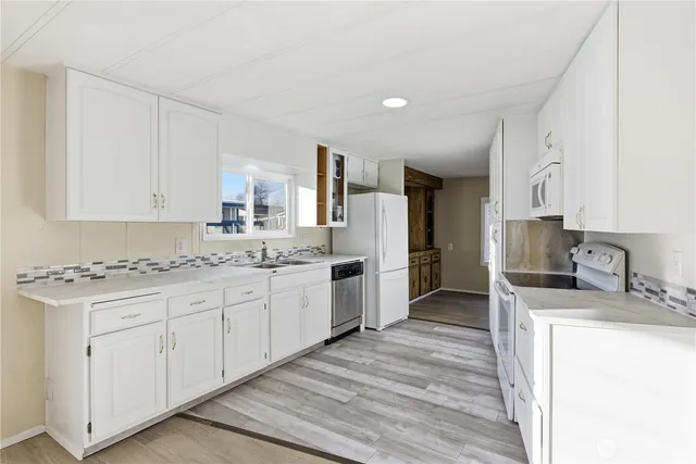 a kitchen with granite countertop a sink stove refrigerator and white cabinets with wooden floor