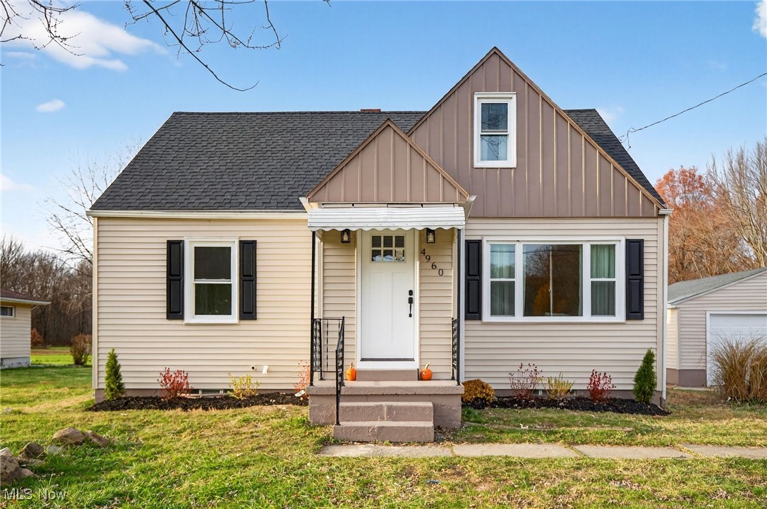 Bungalow-style house with board and batten siding, a front lawn, roof with shingles, and an outbuilding