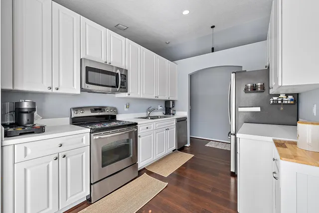 a kitchen with stainless steel appliances granite countertop a refrigerator a stove top oven a sink dishwasher and white cabinets with wooden floor