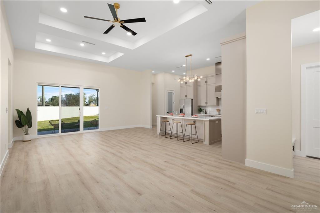 7820 North 38th Street McAllen, TX 78504 - Photo 3 of 31 Unfurnished living room with a chandelier, light wood-style floors, recessed lighting, ceiling fan, and a raised ceiling