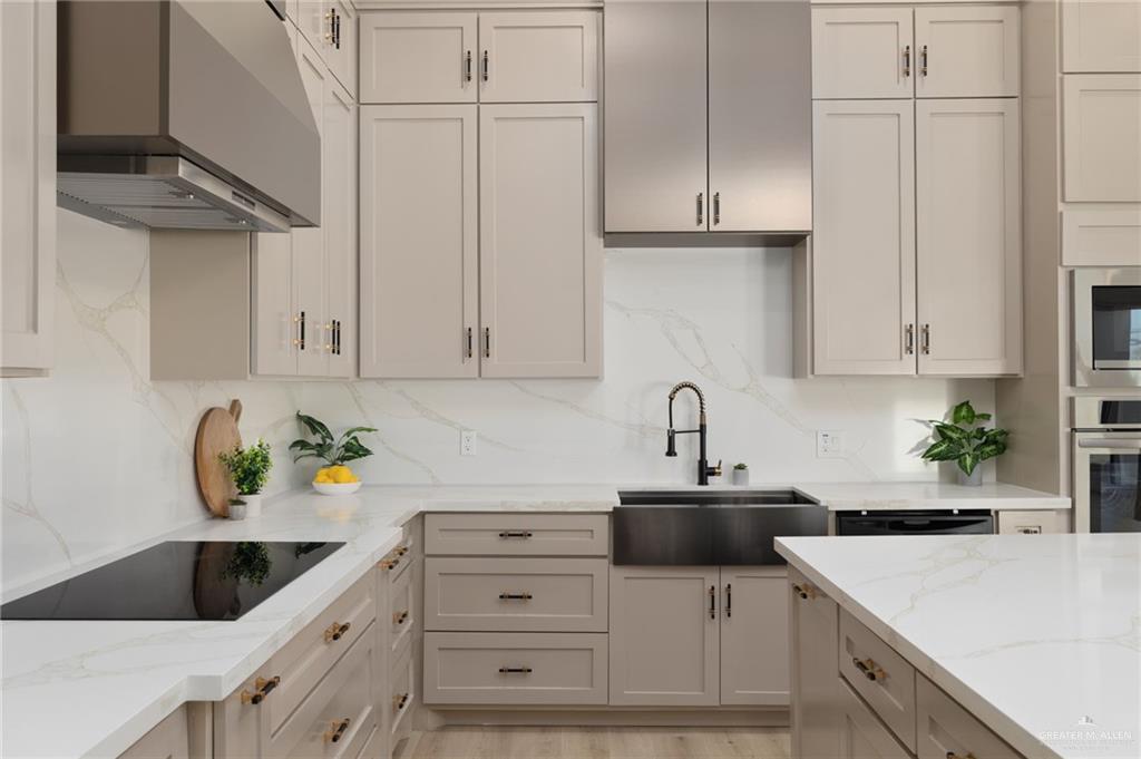 7820 North 38th Street McAllen, TX 78504 - Photo 6 of 31 Kitchen with light stone countertops, wall chimney range hood, stainless steel appliances, light wood-style flooring, and tasteful backsplash