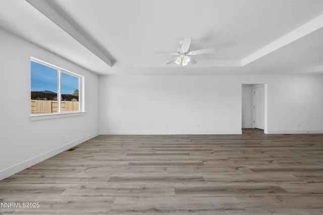 a view of an empty room with wooden floor and a ceiling fan