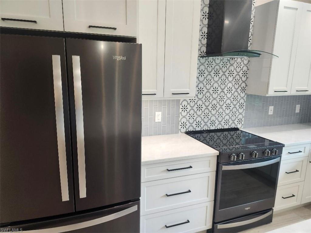512 Raven Way Naples, FL 34110 - Photo 5 of 20 Kitchen with freestanding refrigerator, black electric range oven, wall chimney exhaust hood, and white cabinetry