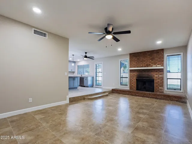 a view of a room with a fireplace a ceiling fan and windows