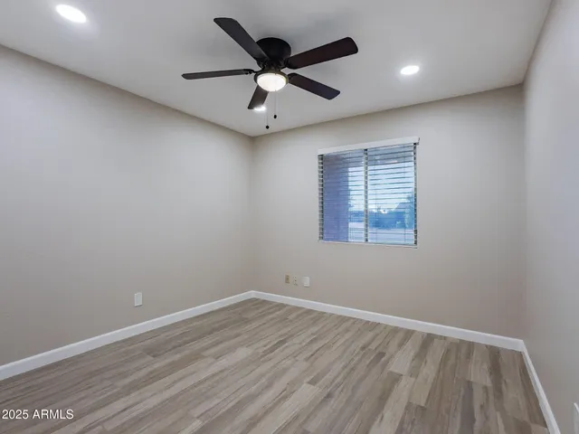 an empty room with wooden floor ceiling fan and windows