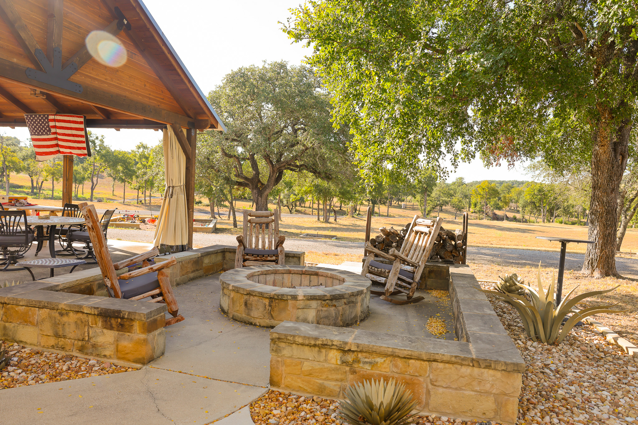 920 Ryan Road Bertram, TX 78605 - Photo 40 of 40 A stone fire pit area sits beside a covered pavilion overlooking a tree-lined landscape.