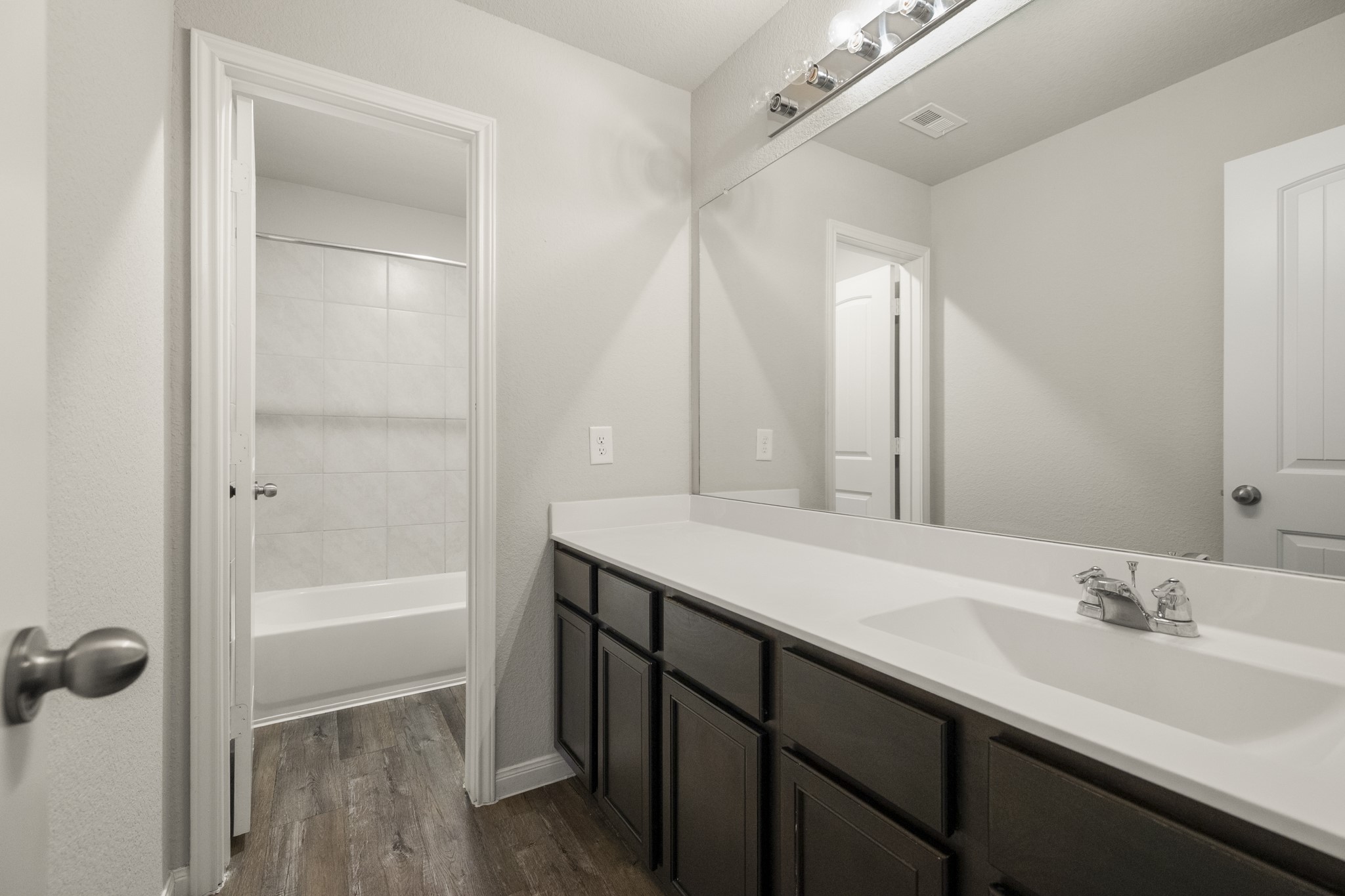 3571 Cannon Drive Conroe, TX 77301 - Photo 22 of 39 2nd level bathroom features a modern design with a spacious double vanity, ample cabinet storage, and a large mirror. It includes a separate area with a bathtub and shower, all complemented by sleek finishes and wood-look flooring.