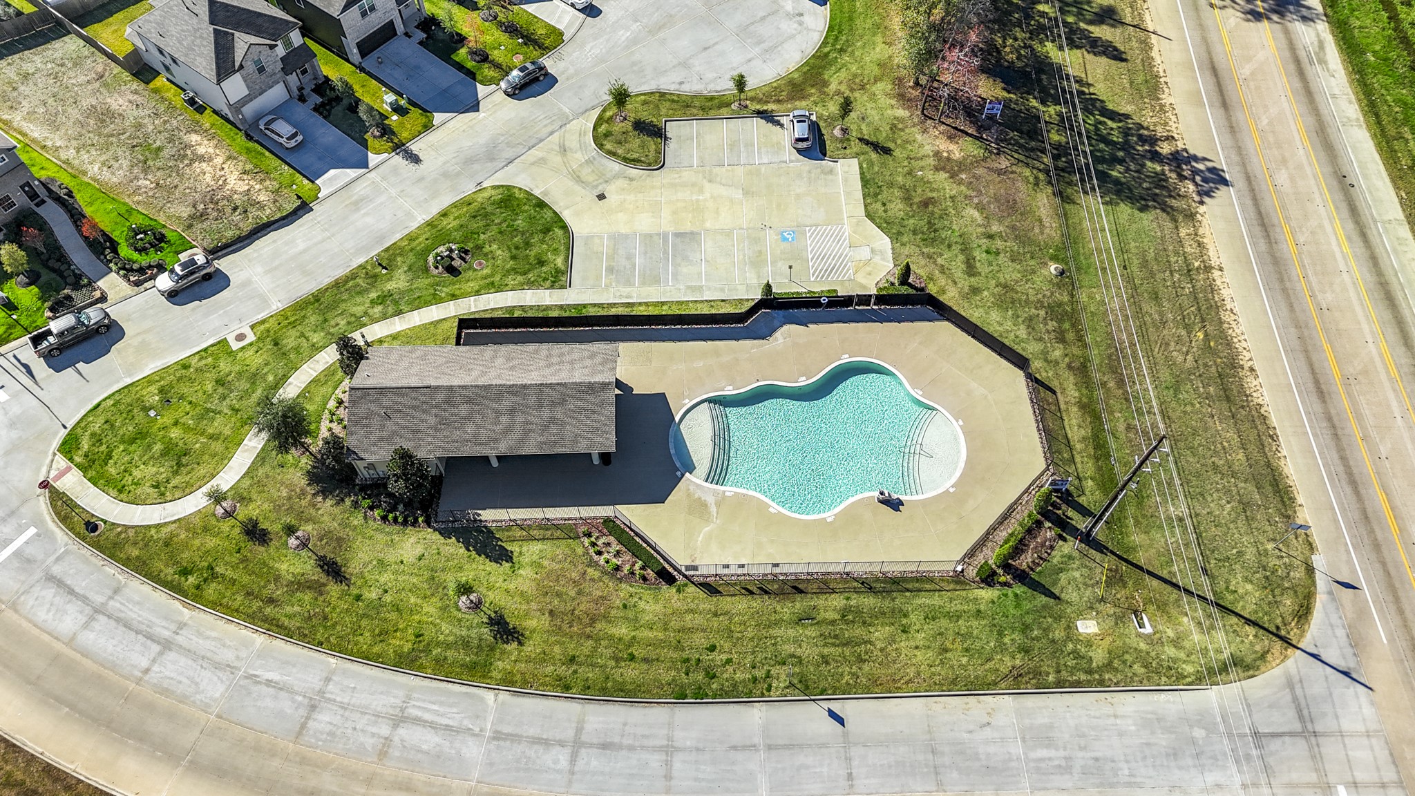 3571 Cannon Drive Conroe, TX 77301 - Photo 31 of 39 This aerial photo showcases a community pool with a distinct shape, surrounded by a paved area and a small building, likely for amenities or storage. The pool is fenced and set within a well-maintained grassy area, with adjacent roads and residential houses nearby. Ideal for families seeking community amenities.