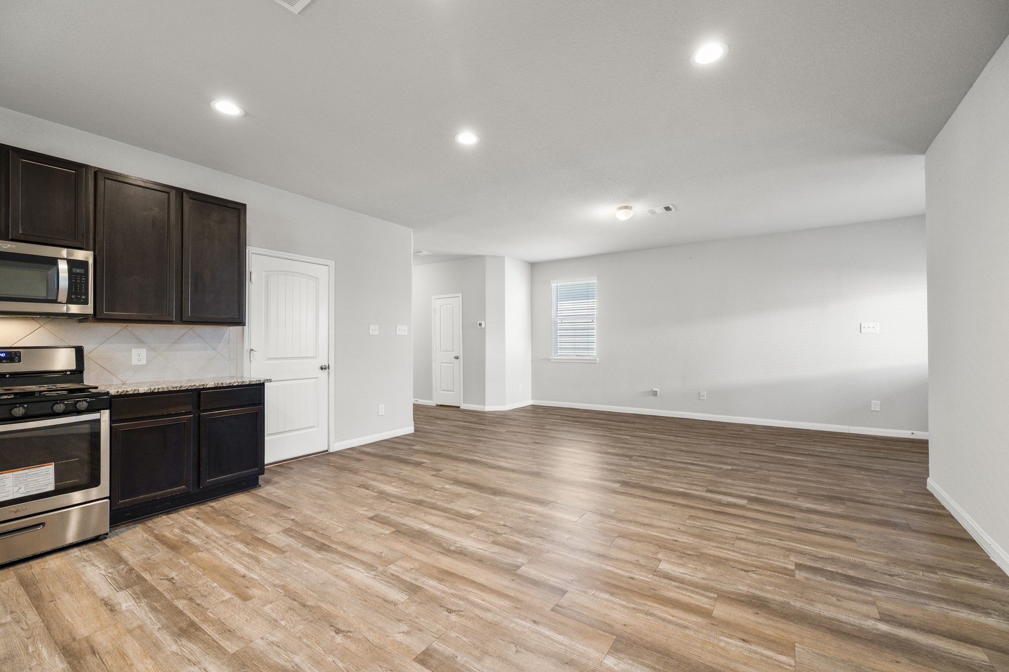 3571 Cannon Drive Conroe, TX 77301 - Photo 4 of 39 This photo showcases a spacious, open-concept living area with sleek hardwood flooring. The kitchen features dark cabinetry, stainless steel appliances, and a modern design. Recessed lighting adds brightness, and the neutral walls offer a versatile backdrop for personalization.