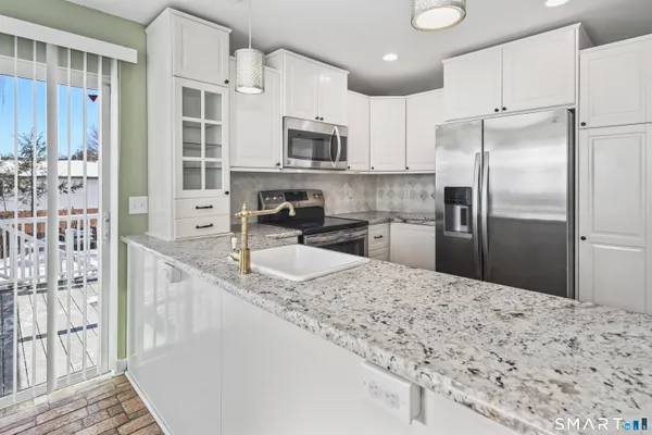 a kitchen with stainless steel appliances kitchen island granite countertop a refrigerator a sink a stove a oven with white cabinets and wooden floor