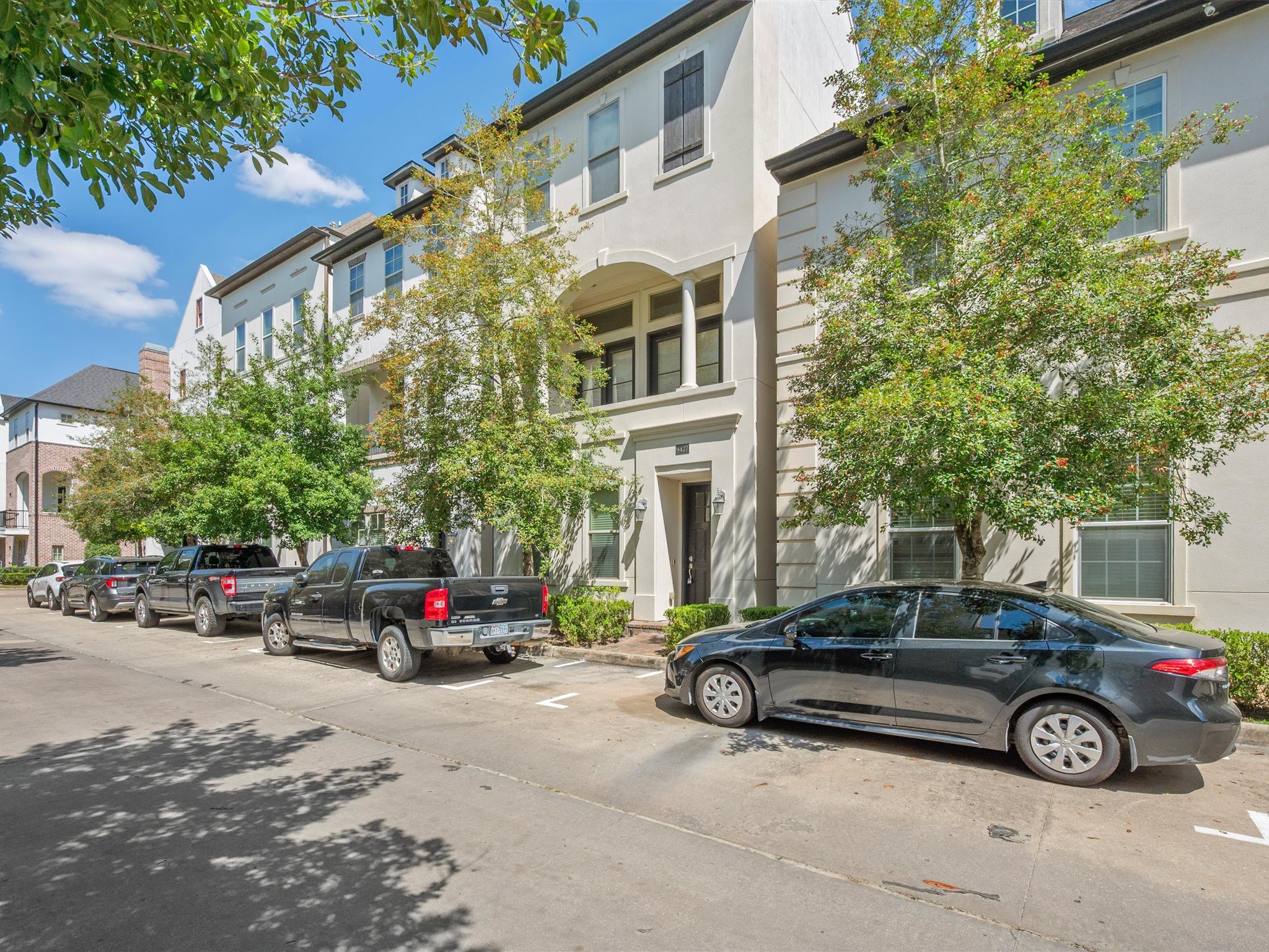 9427 London Bridge Station Houston, TX 77045 - Photo 2 of 30 Discover modern living in this elegant three-story townhouse, featuring a sleek white exterior, large windows, and lush greenery, all nestled in a welcoming neighborhood with ample parking.