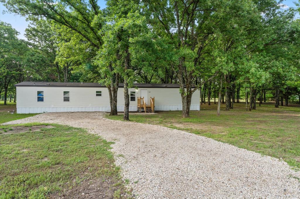 White manufactured home with a dark roof and white skirting, set amidst mature trees
