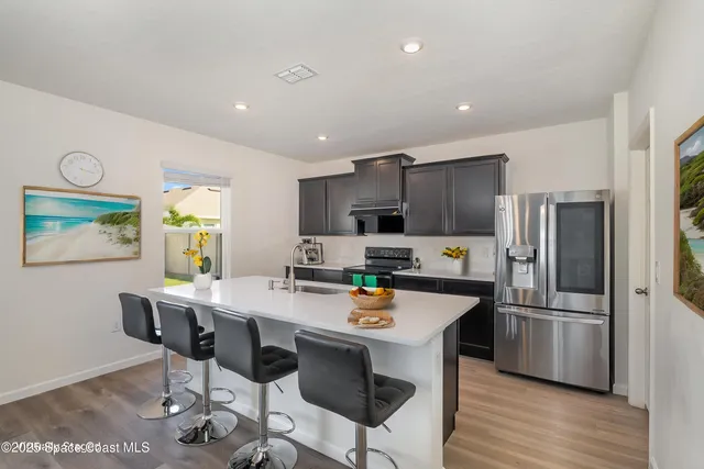 a kitchen with stainless steel appliances a refrigerator a stove a sink a dining table and chairs with wooden floor